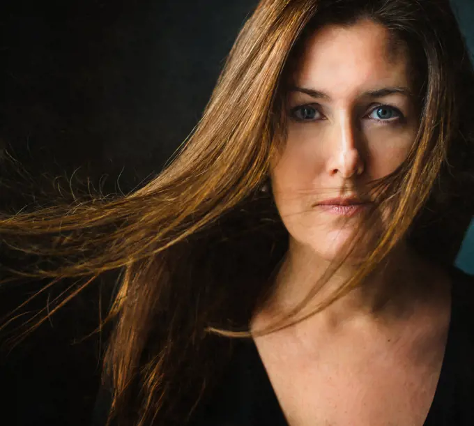 Portrait of a woman with long brown hair blowing across her face.