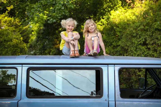 two girls sitting on roof of vintage car laughing and smiling