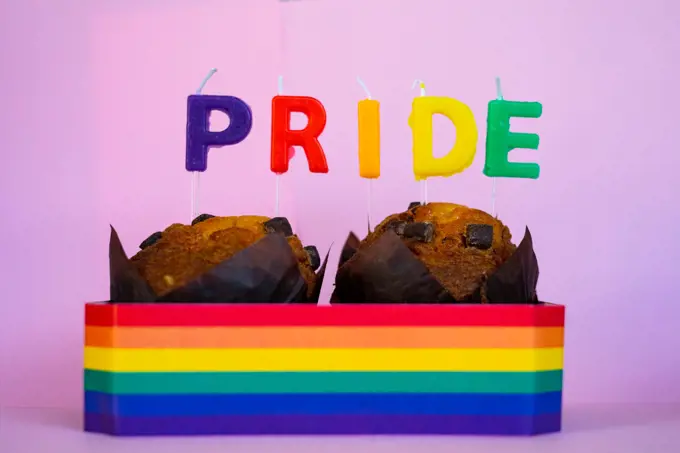 Two muffins with candles and Pride flag.