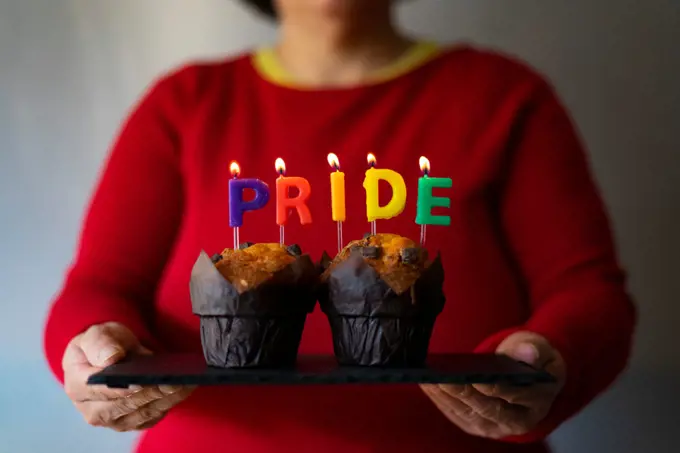 Woman picking up a plate with muffins and Pride candles.