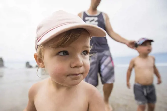 Portrait of cute one year old girl at the beach with brother and dad.