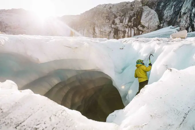 Side view of man ice climbing outside of glacial cave.