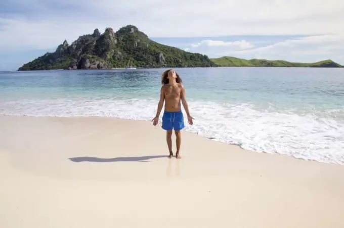 One male tourist, wearing blue swuimsuits, meditating on idyllic beach