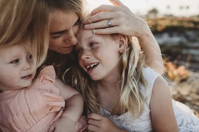 Portrait of mother cuddling with young daughters at beach sunset