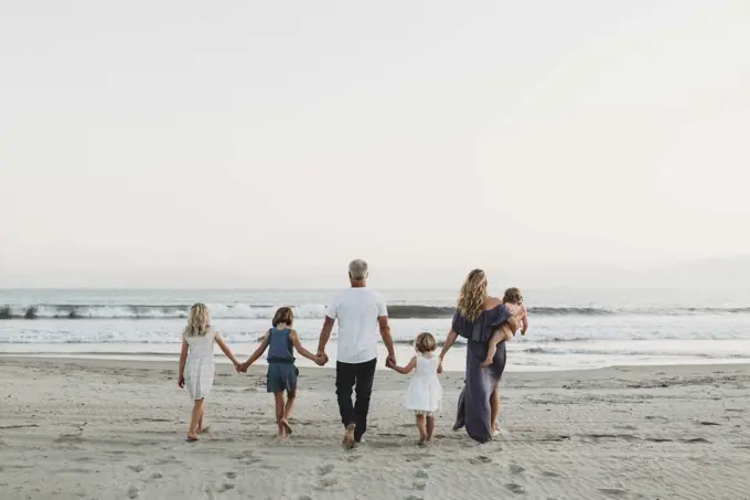 Behind view of young family walking towards the ocean at sunset