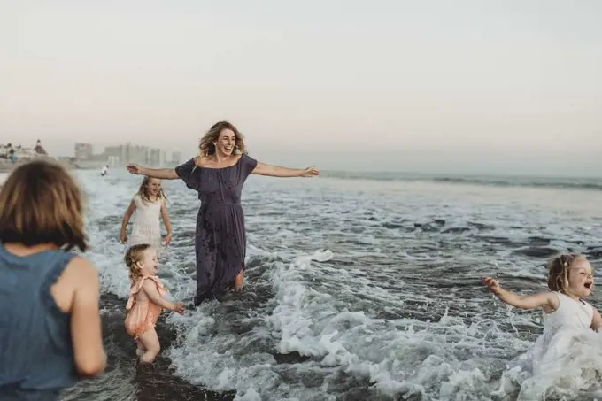 Strong mother with four daughters playing in ocean at sunset