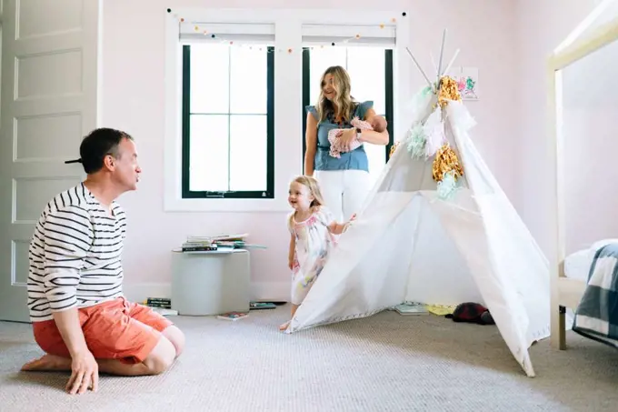 A family of four play together in a child's room with a modern tipi