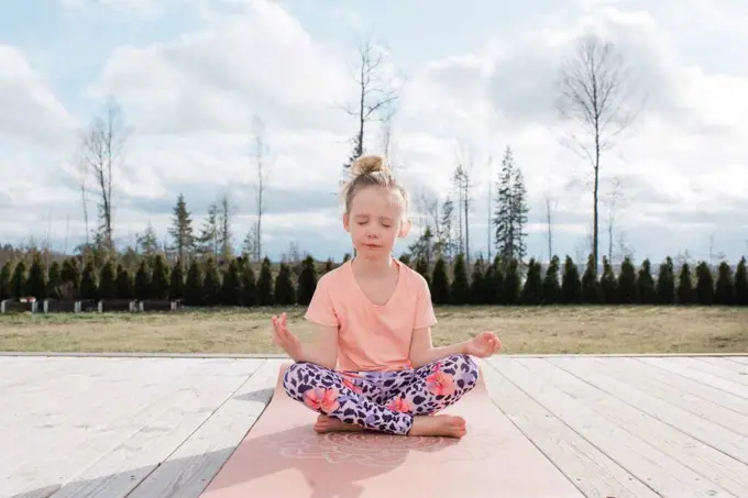 young girl meditating doing yoga in her back yard at home