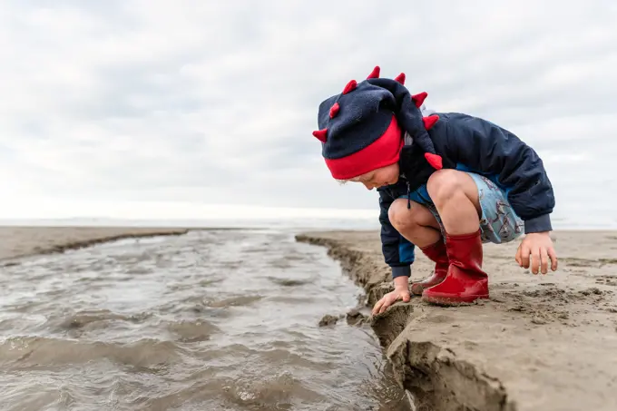 Little kid in boots playing with sand in New Zealand