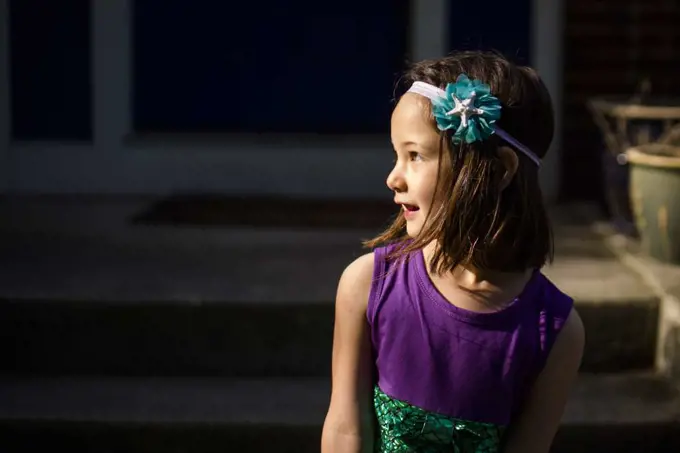 A beautiful little girl in a headband looks over her shoulder smiling