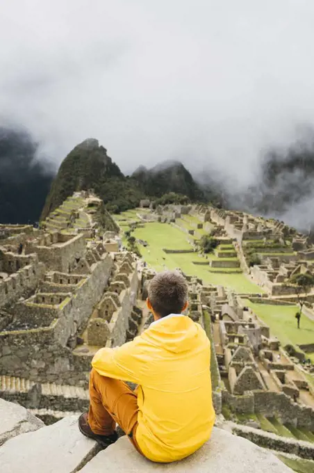 A man in a yellow jacket is sitting near ruins of Machu Picchu, Peru