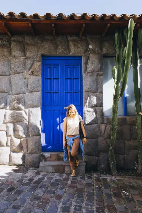 A young woman is standing near a blue old door in Cusco, Peru