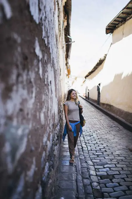 A young woman is standing near an old wall in Cusco, Peru