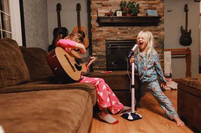 Young girls singing loudly and playing guitar in living room