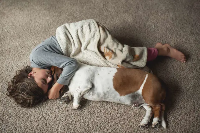 Young girl laying on the floor in blanket with basset hound dog