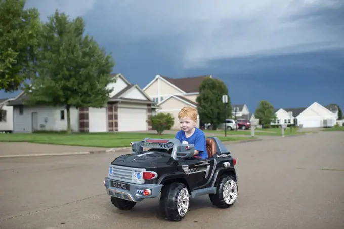 Young boy drives electric toy car down neighborhood street