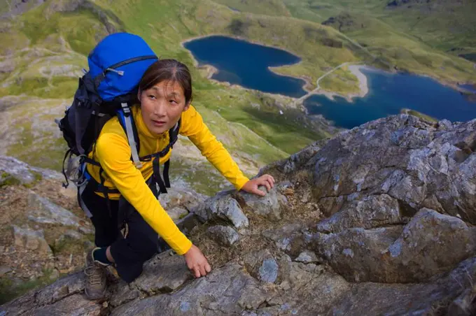 woman with rucksack scrambling up Snowdonia mountain