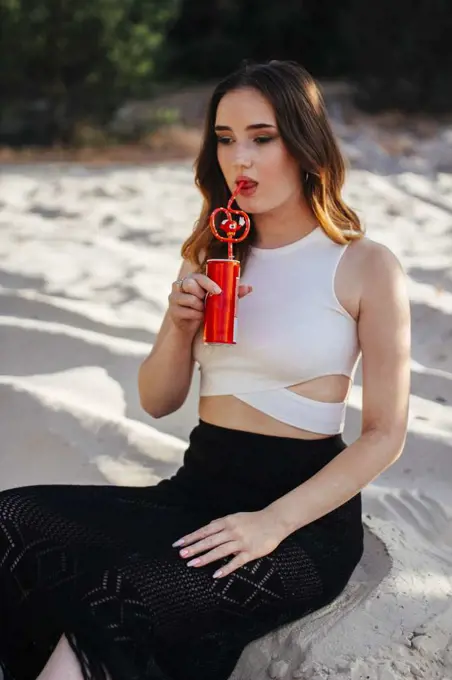 Woman drinking a drink from an iron can by taking a straw in her mouth