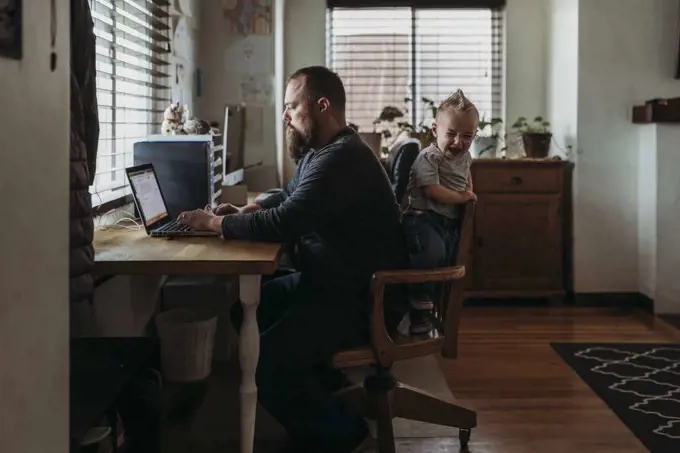 Dad working from home with one year old boy crying while he works