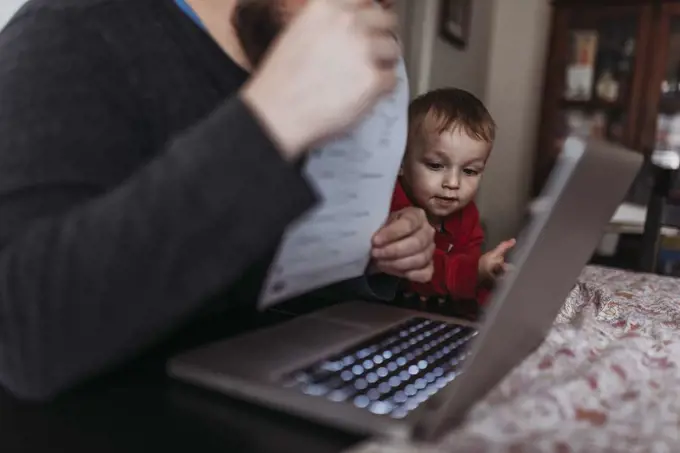 Close up of young son looking at dads computer while he works at home