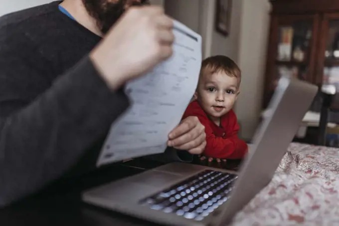 Close up of young son looking at dads computer while he works at home