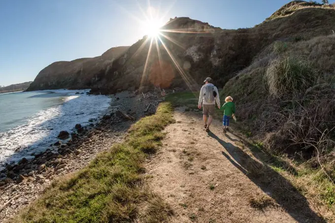 Dad and small child holding hands on path near ocean on a sunny day