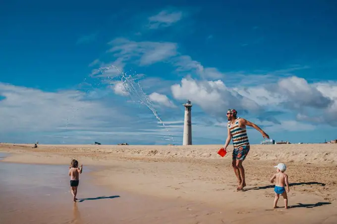 Kids playing with water at the beach with their dad on a sunny day