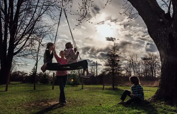 Children playing outside on a tire swing at sunset