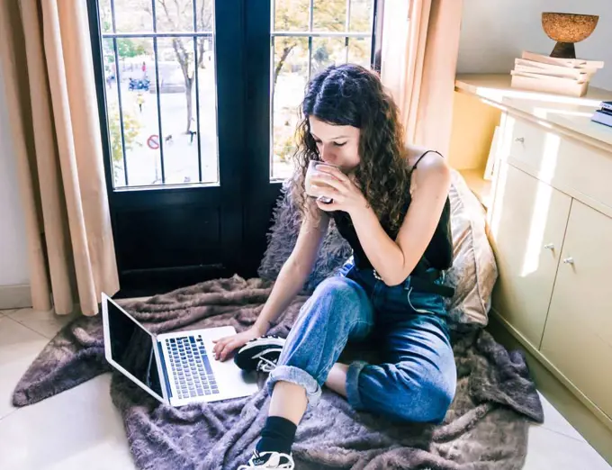 young girl working at home with laptop next to the window