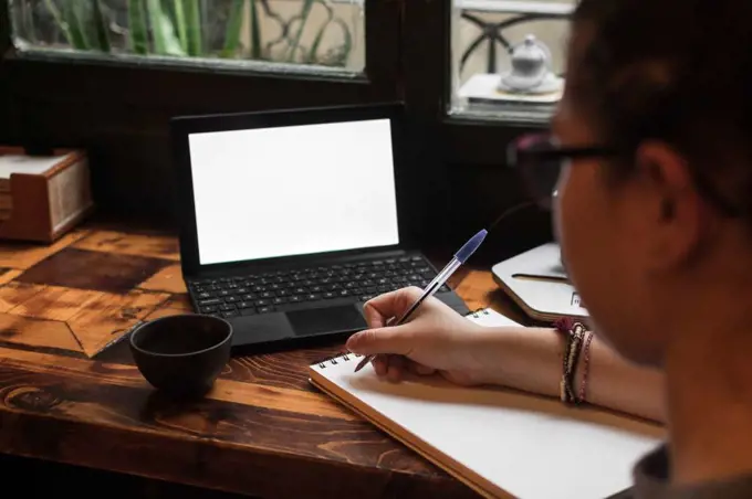 A young student works on a table near a pub window. Close up view