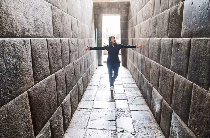 Woman stretching her arms between ancient Inca walls, Cusco, Peru