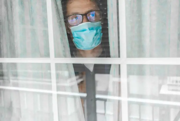 Middle-aged man in the medical mask is quarantined in the hospital and pressed her forehead against the window