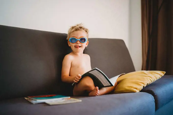 Male child reading topless with goggles and sticking his tongue out