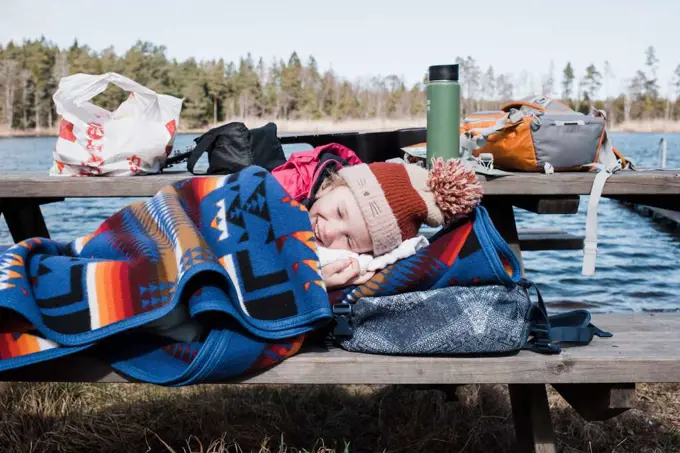 young child laying down on a bench wrapped up in a blanket