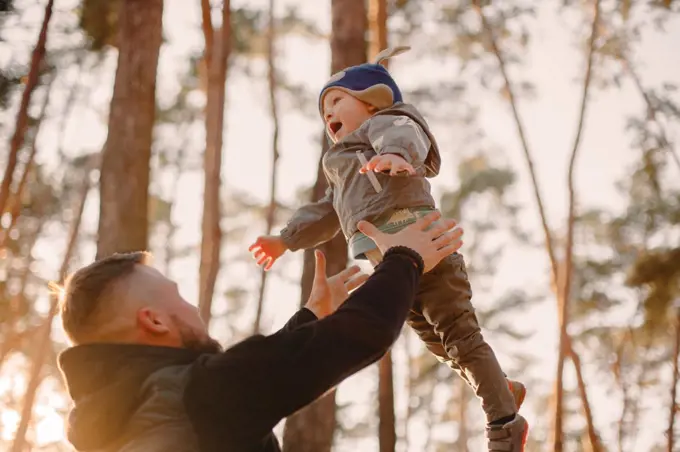 Father throwing son in air while playing in forest