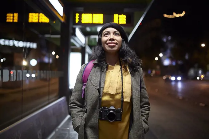 woman standing with a camera waiting at the bus station at night