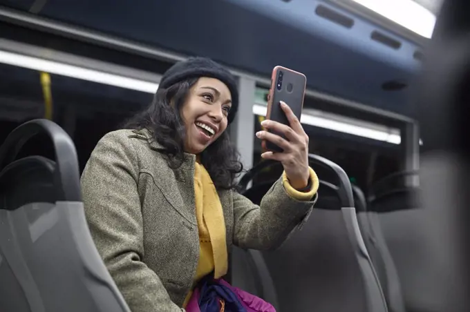 Smiling woman sitting and using his cellphone in a public bus at night