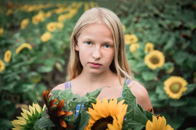 Serious Young Girl Holding Sunflowers with Sunflowers in Background