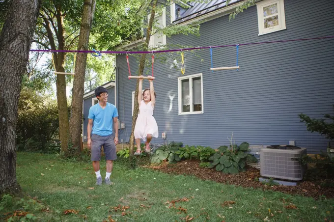 a cute girl hangs from a bar while her proud smiling father watches