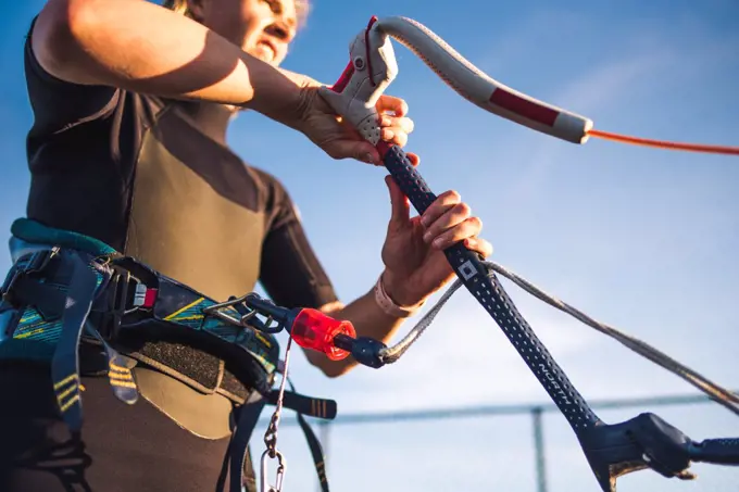 A woman in a wetsuit rigs up her kite on the beach before kiteboarding