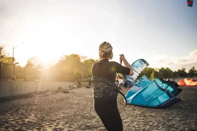 A woman in a wetsuit rigs up her kite on the beach before kiteboarding