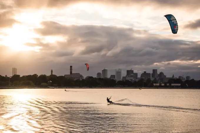 A woman kiteboarding on a summer evening with a dark Boston skyline