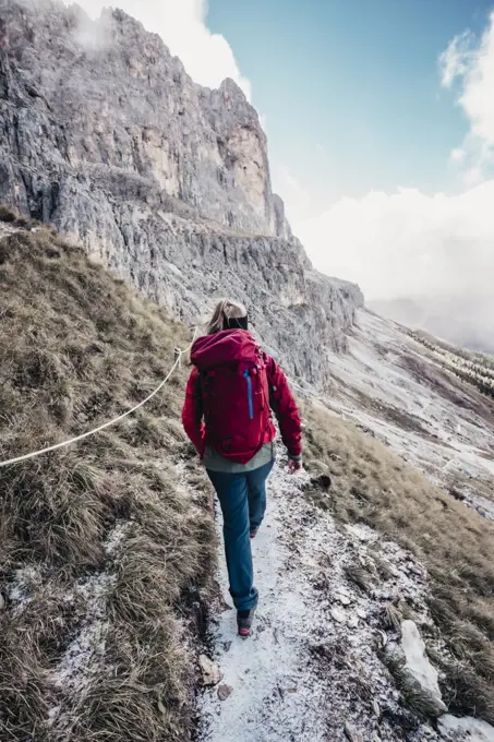 Young female mountaineer hikes towards rock face in Italian Dolomites