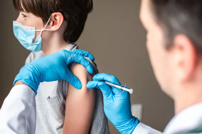 Child wearing mask getting vaccinated by doctor holding a needle.