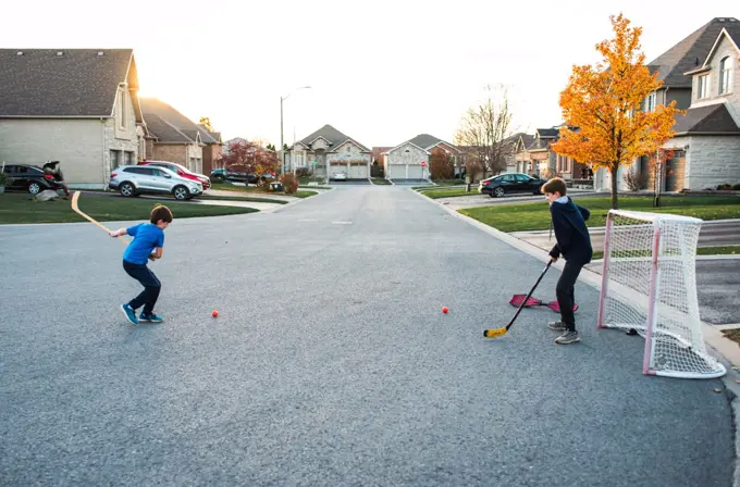 Two boys playing street hockey on a residential street in the fall.