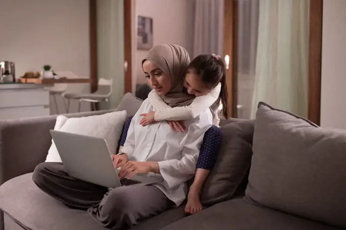 Muslim mother with daughter working on couch