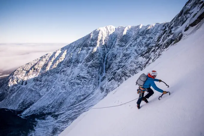 Alpine climber ascending steep snow with mountains behind