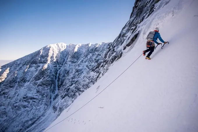 Alpine climber ascending steep snow with mountains behind