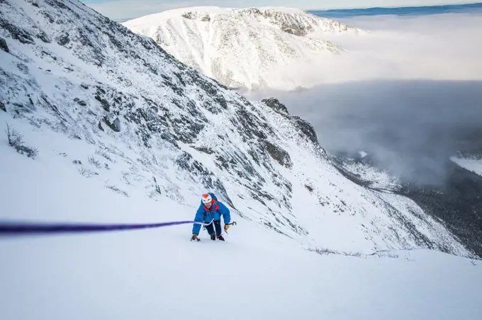 Male climber being belayed up steep snow with cloud inversion behind