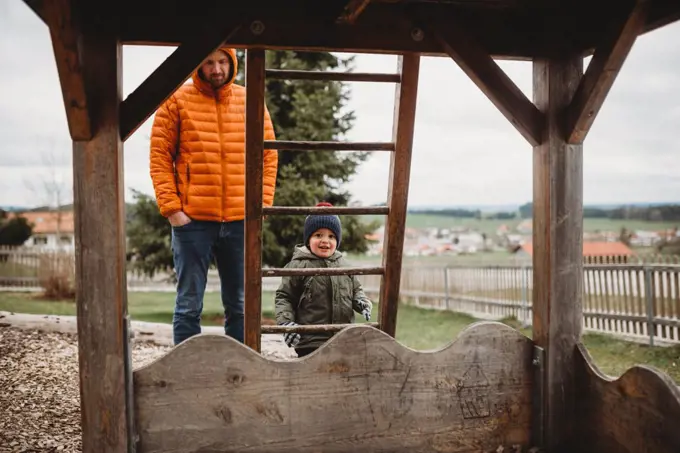 Dad and son at playground in winter climbing ladder to wooden house